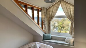 Ein Schlafzimmer mit schrägverdeckter Decke, einer Sitzbank mit Kissen und einem Bett mit Bettdecke und Kissen.