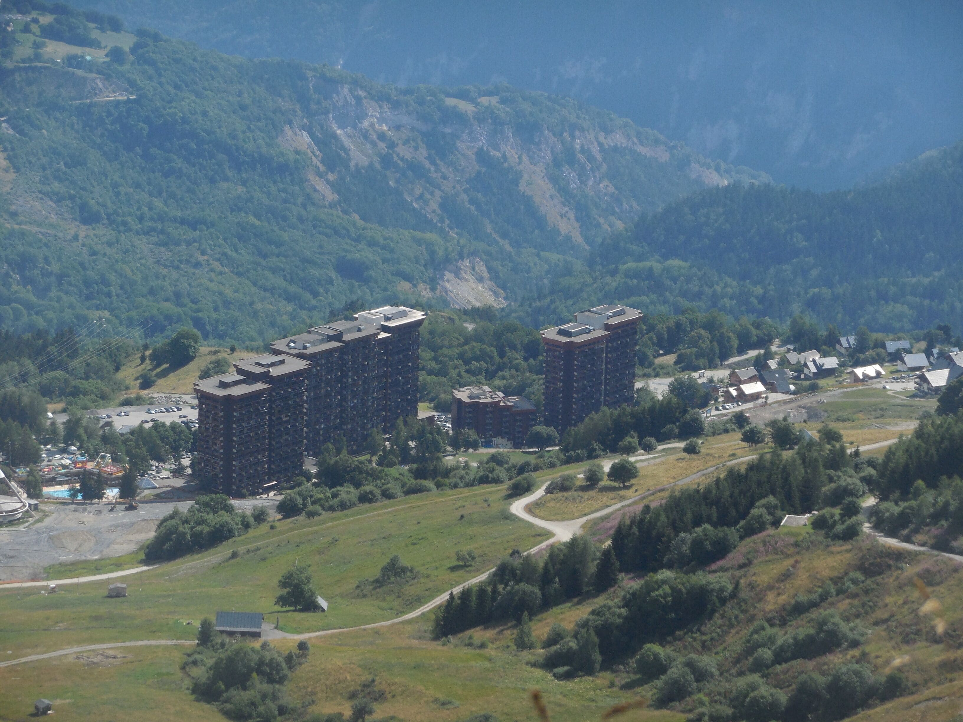 A high-rise building with multiple floors, surrounded by a hilly landscape with greenery and a few scattered houses.