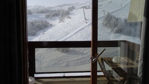 Uitzicht vanuit een kamer met een groot raam op een besneeuwd berglandschap met skiliften.