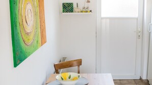 Comedor con mesa blanca, sillas de madera, un bol con limones y un tapete verde.