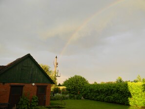 Un bâtiment écologique, avec une base en briques, un petit jardin et un ciel dégagé où l’on peut apercevoir un arc-en-ciel.