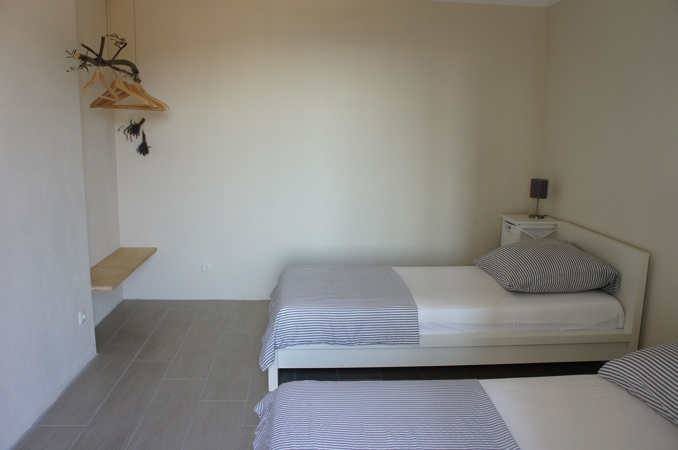 Quarto pequeno e limpo com duas camas, mesa de cabeceira, luminária e cabideiro.