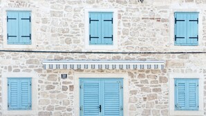 Un edificio in pietra con una porta centrale e quattro finestre con persiane blu.