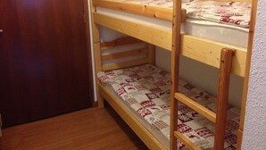 A bunk bed with three levels, wooden railings, and patterned bedding. - Super equipped Studio Apartment with high speed internet (Samoëns)