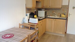 A compact kitchen with wooden cabinets, a microwave, a toaster, and a sink. - Super equipped Studio Apartment with high speed internet (Samoëns)