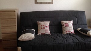 A dark-colored sofa with two decorative pillows, a wooden cabinet, and a mirror on the wall. - Super equipped Studio Apartment with high speed internet (Samoëns)