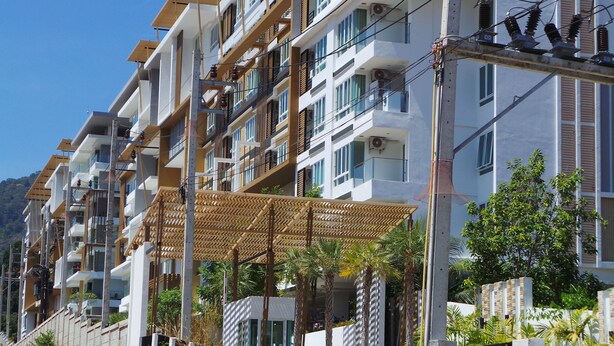 A multi-story residential building with balconies, a covered walkway, and surrounding greenery.