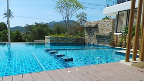 A swimming pool with blue tiles, a wooden deck, and a stone wall.