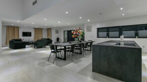 Ein modernes Wohnzimmer mit Essbereich, ausgestattet mit einer großen Kochinsel mit Spüle, einem flachbildfernseher an der Wand und einem großen Fenster mit Aussicht.