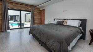 Ein modernes Schlafzimmer mit einem großen Bett, Blick auf einen Swimmingpool und einer Glastür zum Außenbereich.