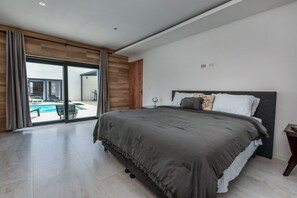A modern bedroom with a large bed, a view of a swimming pool, and a sliding glass door leading to an outdoor area. - Design Villa Maria at Aruba (Noord)