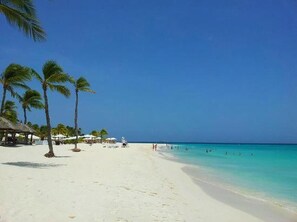Una playa con arena blanca, palmeras y agua azul cristalina.