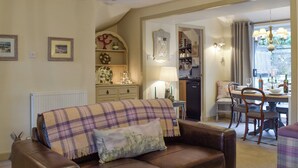 Un salon chaleureux avec un canapé en cuir marron, un plaid douillet et un coin repas avec une table mise pour deux personnes.