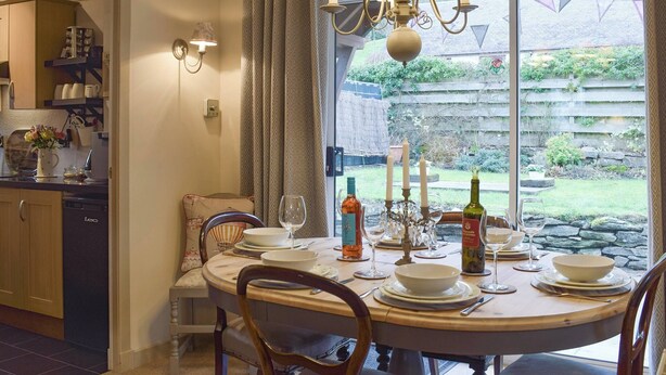 Un coin repas avec une table ronde dressée pour quatre personnes, un lustre et une vue sur le jardin grâce à de grandes fenêtres.