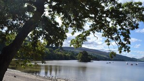 Une vue sur un lac, avec une rive rocheuse, des bateaux sur l’eau et une colline boisée en arrière-plan.