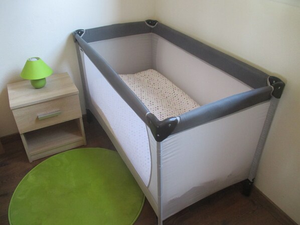 A baby crib with a grey frame and white mattress, a green floor mat, and a wooden nightstand with a green lamp.
