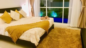 Ein Schlafzimmer mit einem großen Bett, einem Fenster mit Vorhängen und Blick auf Grünfläche.
