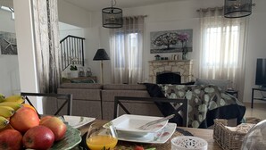 Zona pranzo con tavolo in legno apparecchiato per la colazione, con frutta, bicchieri di succo d'arancia e pane.