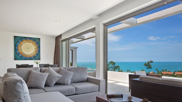 A modern living room with a grey sectional sofa, a wooden coffee table, and a view of the ocean.