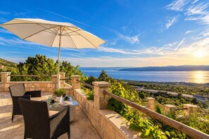 An outdoor seating area with a table, chairs, and an umbrella, overlooking a scenic view of a body of water and hills. - Villa with heated Swimmingpool, barbecue , terrace with sea view, up to 6 people (Baska Voda)