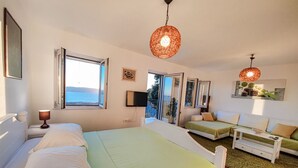 A bedroom with a bed, a sofa, a TV, and a balcony with a view.