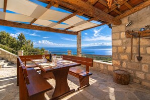 Ein Essbereich im Freien mit einem Tisch für zwei Personen, mit Blick auf eine malerische Aussicht auf das Meer und die Berge.