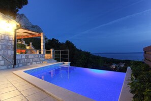 Una piscina con vistas al mar y a las montañas al atardecer.