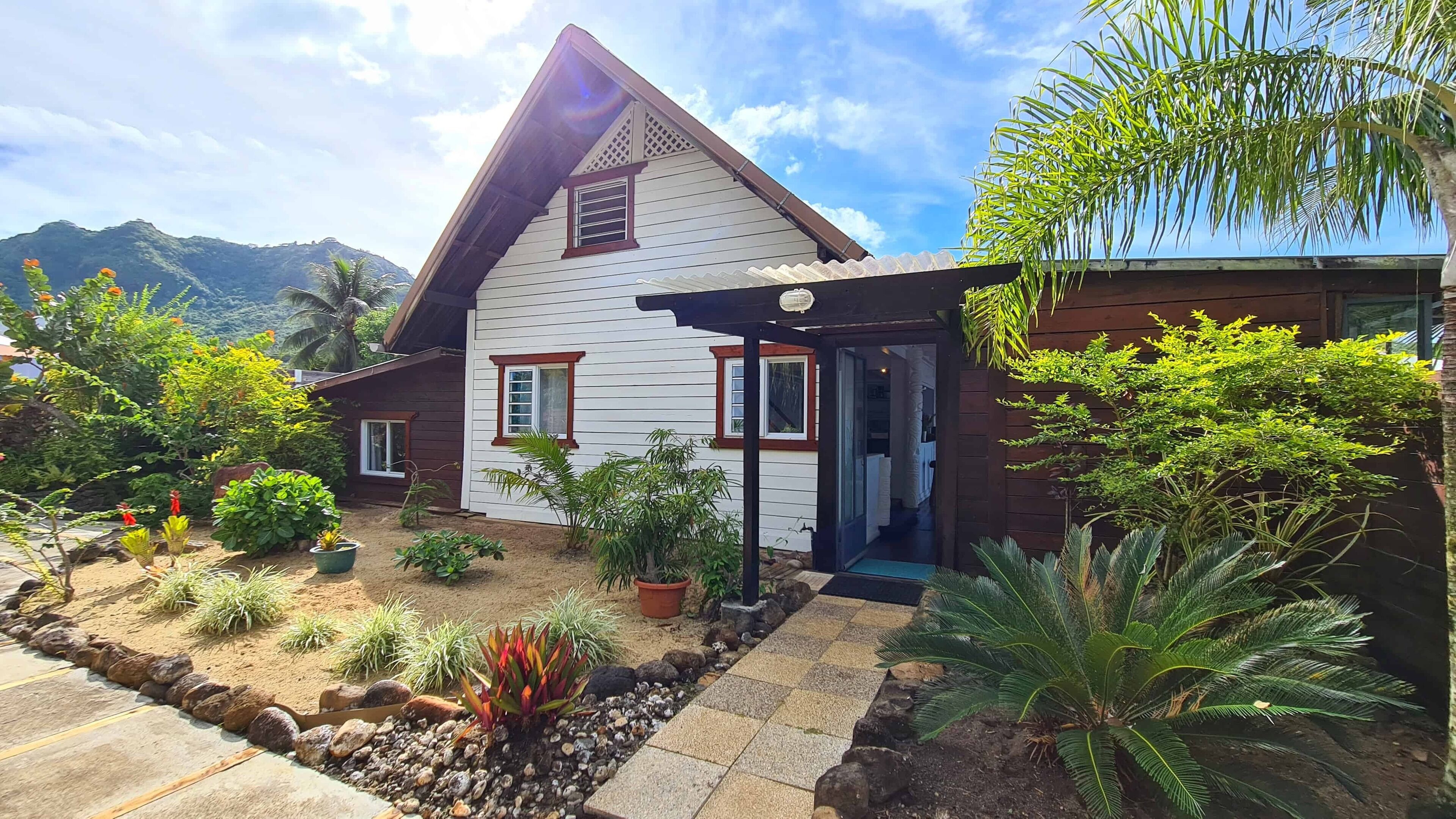 A house with a sloped roof, a porch, and a garden with various plants and rocks.