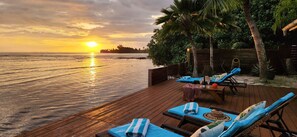 A wooden deck with lounge chairs and a table, overlooking a calm sea and a sunset. - Modern villa with pool by the sea on the island of Moorea ('Atiha)