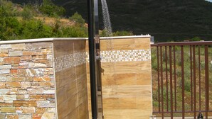 A stone and tiled shower enclosure with a metal gate, set against a mountainous backdrop.