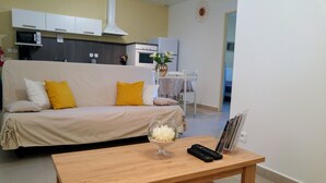 A living room with a sofa, a coffee table, a vase with flowers, and a remote control.