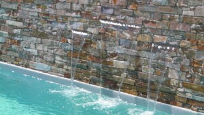 A swimming pool with a stone wall and water cascading down.