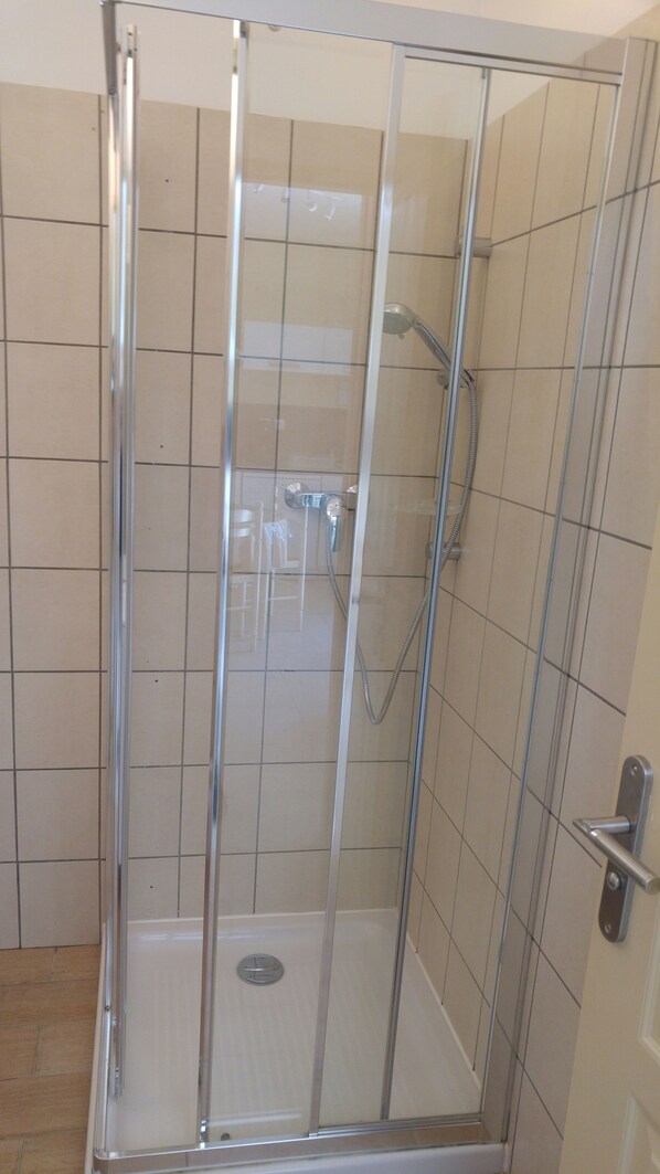 A glass-enclosed shower stall with a showerhead and control panel.