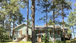 A two-story cabin with a front porch, surrounded by tall pine trees.