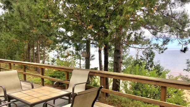 A deck with a table and chairs, overlooking a body of water and surrounded by trees.