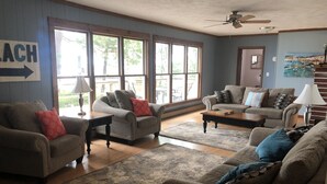 A living room with two sofas, a coffee table, and a rug. There are large windows and a ceiling fan.