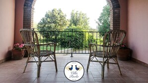 A patio with two wicker chairs and a table, an archway, and a view of greenery. - Castiadas, typical Sardinian private villa with swimming pool and garden (Castiadas)