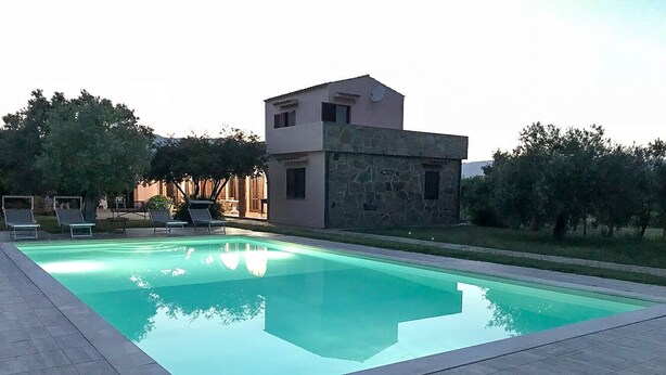 A rectangular swimming pool with lounge chairs and a stone building with a flat roof. - Castiadas, typical Sardinian private villa with swimming pool and garden (Castiadas)
