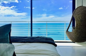 Enjoy ocean views from the comfort of this bedroom, featuring a bed and a wicker chair.