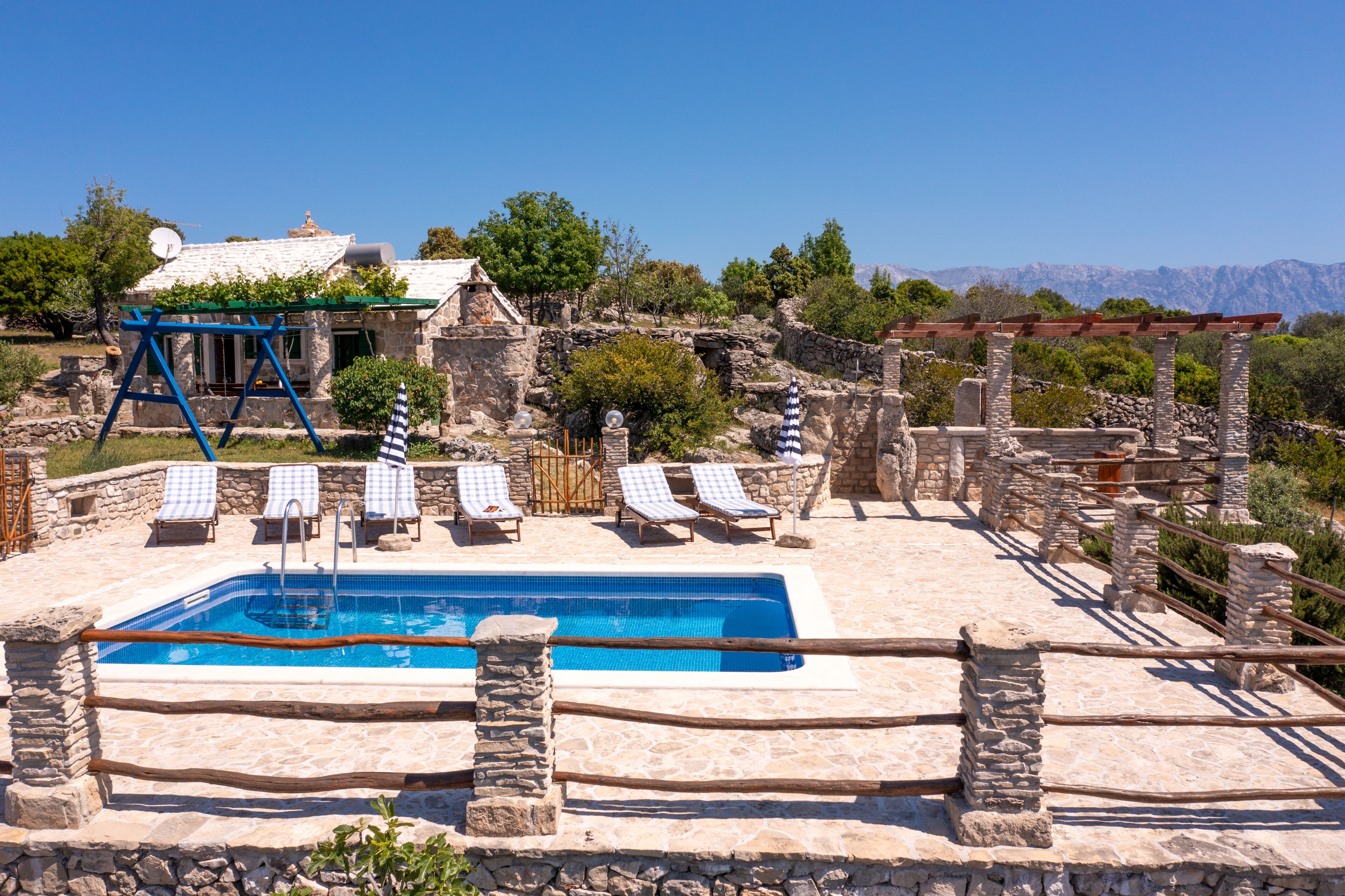A stone pool with lounge chairs, a pergola, and a view of mountains.