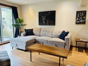A modern living room with a sectional sofa, a wooden coffee table, and a large window with curtains.