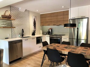 Une cuisine moderne avec un coin repas, équipée d’un lave-vaisselle, d’un four, d’un réfrigérateur et d’un crédence décorée.