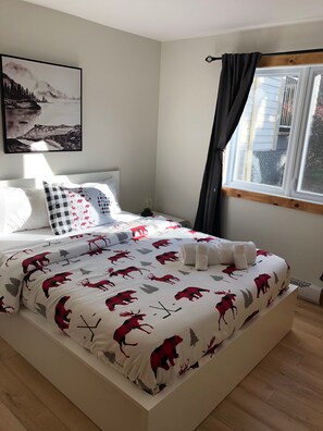 Una cama bien hecha con una colcha estampada, una lámpara de noche y una ventana con cortinas.