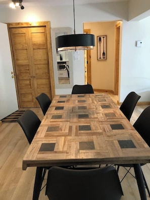 A dining area with a wooden table and black chairs, a black pendant light, and a wooden door.