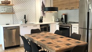 Una cucina moderna con isola centrale, sedie nere, un tavolo da pranzo in legno e un frigorifero in acciaio inossidabile.