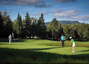 Un parcours de golf avec un ciel dégagé, des arbres et des montagnes en arrière-plan.