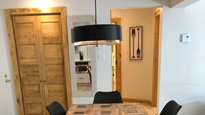 Zona pranzo con tavolo in legno e sedie nere, una lampada a sospensione nera e una porta in legno.
