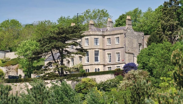 Stately building with a classical facade, surrounded by lush greenery and mature trees.