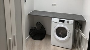Une buanderie équipée d’un lave-linge, d’un étendoir et d’un plan de travail gris.