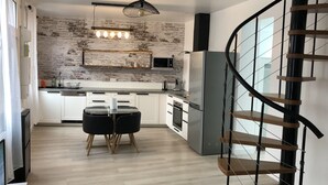 Une cuisine moderne avec un mur de briques en guise de crédence, un coin repas doté d’une table en verre et un escalier en colimaçon.